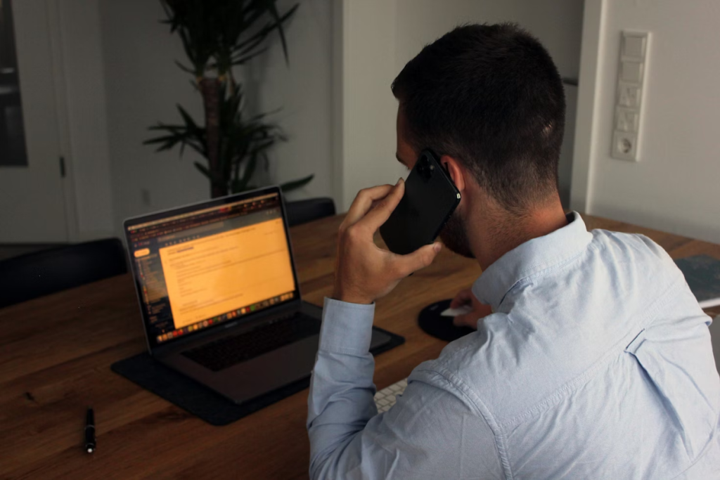 Business professional making a phone call while reviewing accounts receivable reports on his laptop