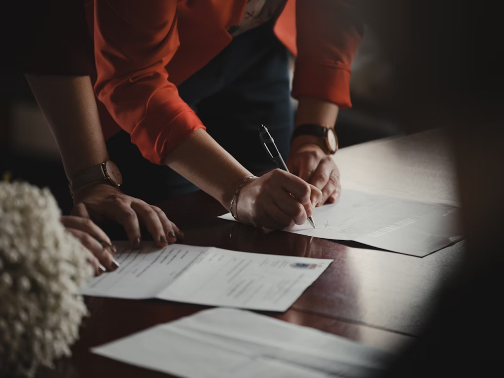 Business professionals signing printed documents on a wooden desk
