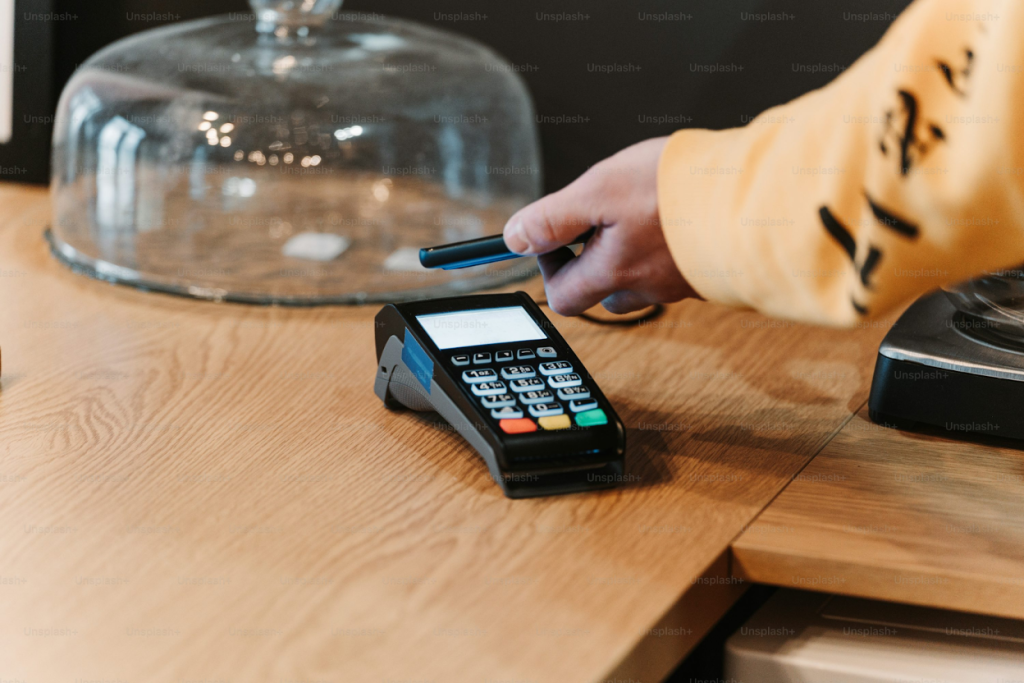Hand holding a payment card near a card reader terminal.