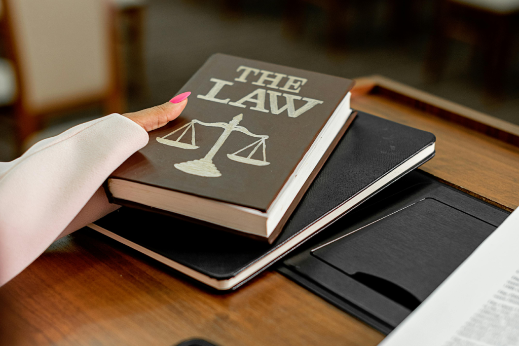 Hand holding law book with scales of justice on cover atop notebooks on desk