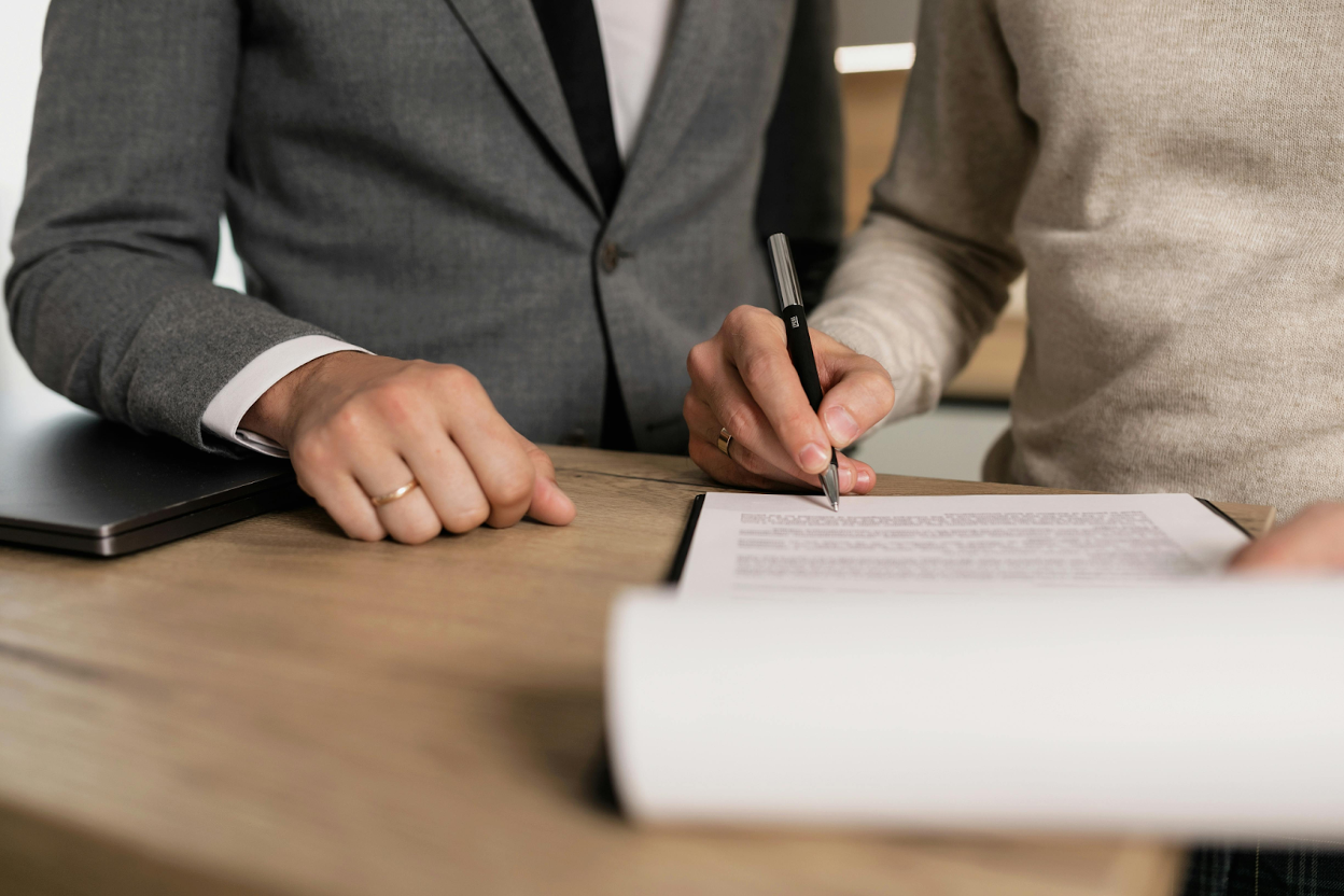 Two people review and sign a business contract at a desk