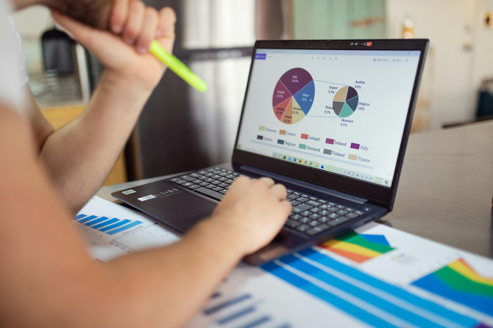 A person analyzing pie charts and financial graphs on a laptop and printing reports.