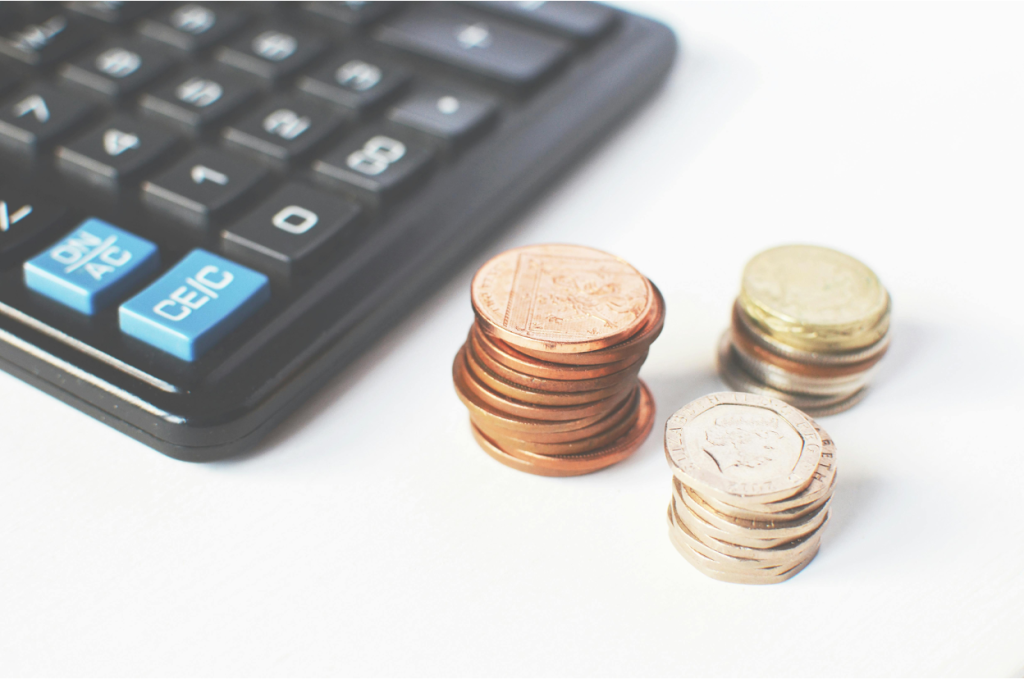 Calculator with blue function keys next to three small stacks of coins on a white surface.