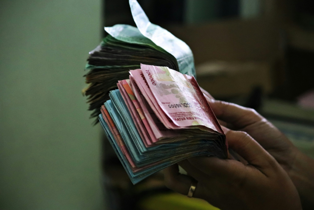 Hands holding thick stacks of currency bills in various denominations against a blurred background