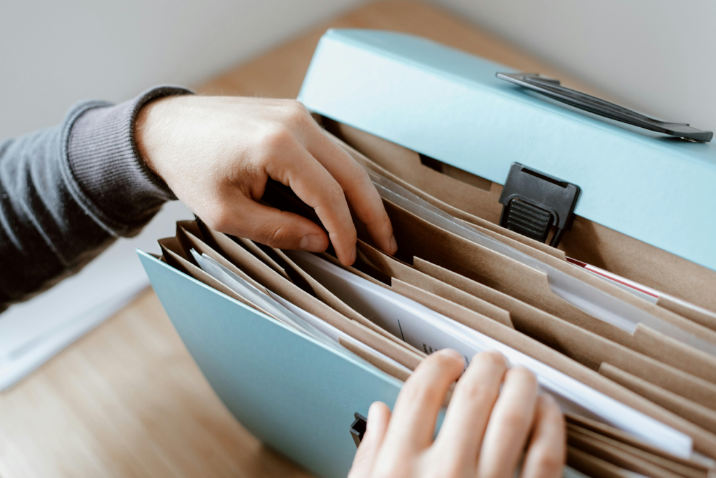 Hands reaching into a light blue desktop file organizer containing multiple manila folders.