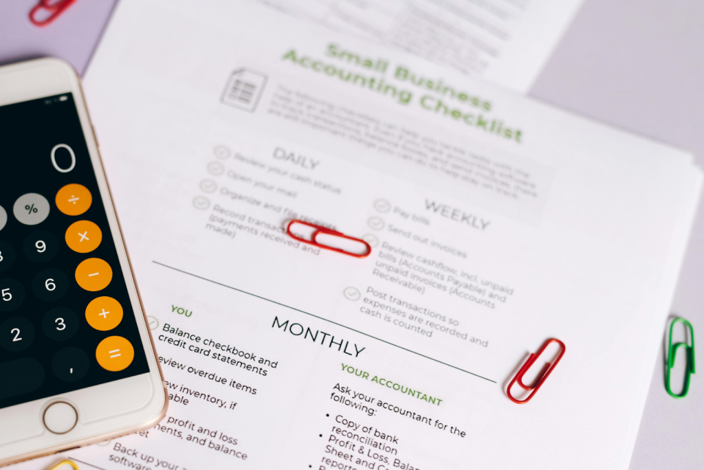 Small business accounting checklist with a smartphone calculator and paperclips.