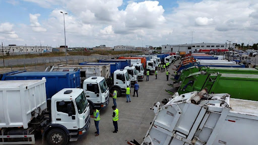Waste management trucks lined up at a commercial facility with workers in safety vests.